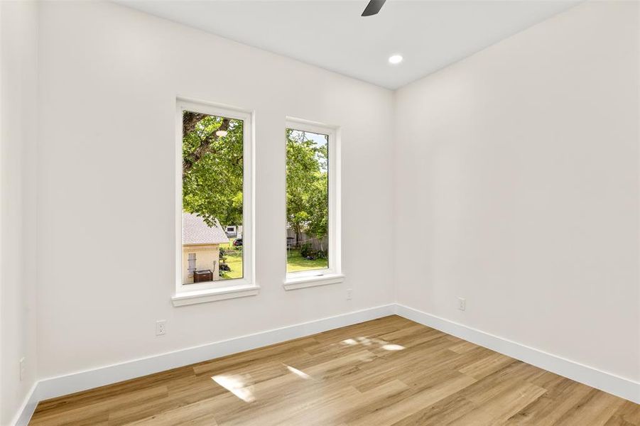 Neutral-toned room featuring two tall, rectangular windows, wood-finish flooring, recessed lighting, and a ceiling fan