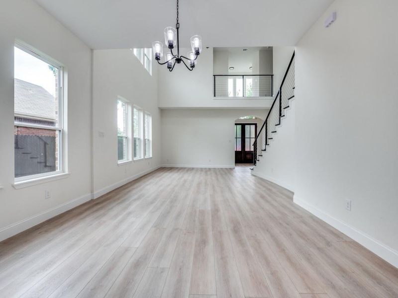 Unfurnished living room with a chandelier, stairway, light wood-style floors, baseboards, and a towering ceiling