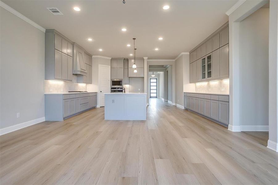 Kitchen with crown molding, a kitchen island with sink, light hardwood / wood-style floors, and gray cabinets