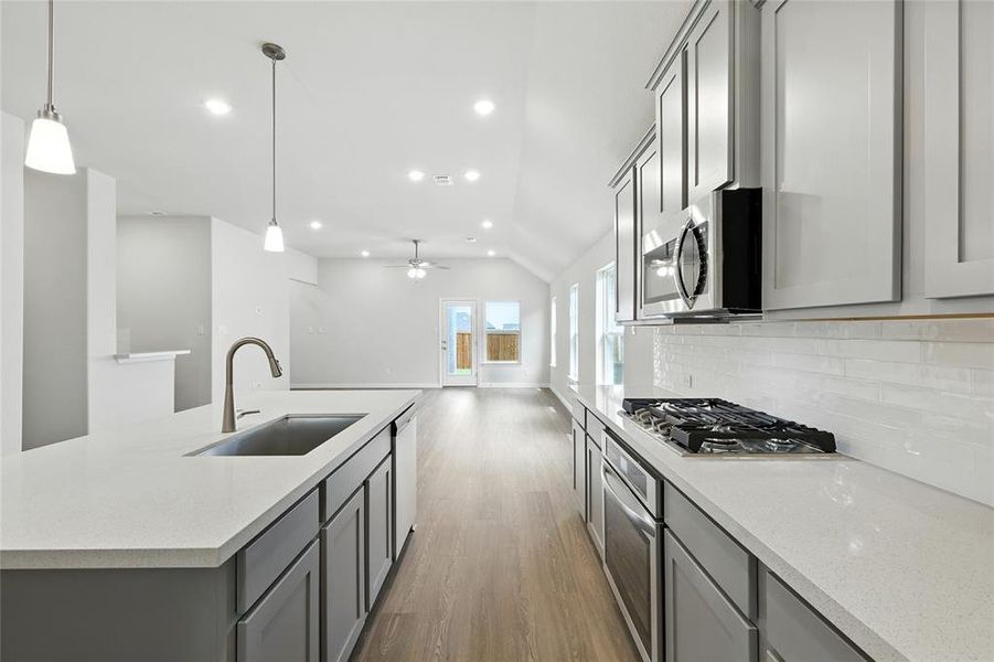 Kitchen with gray cabinetry, light wood-style floors, lofted ceiling, stainless steel appliances, and backsplash