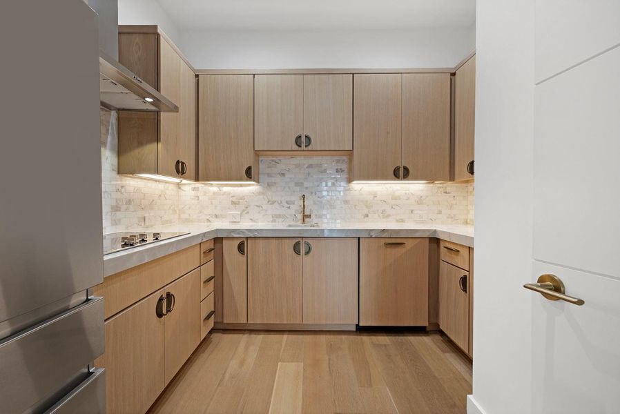 Well-appointed kitchen featuring light wood cabinetry, a tiled backsplash, and under-cabinet lighting