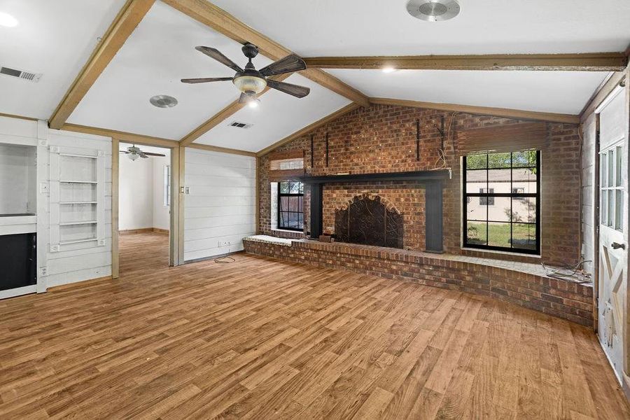 Living room with a brick fireplace, light wood-style flooring, brick wall, and a ceiling fan