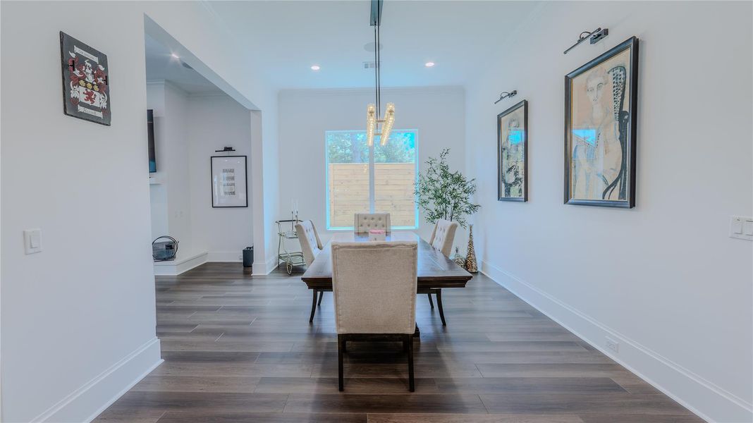 This photo showcases a bright dining area with modern decor. It features a wooden floor, a rectangular dining table with upholstered chairs, contemporary artwork, and a large window that allows natural light to fill the space.