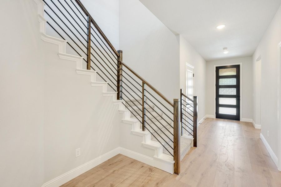 Entryway with white staircase, metal railing, light wood floors, and black front door with glass panels Entryway with white staircase, metal railing, light wood floors, and black front door with glass panels