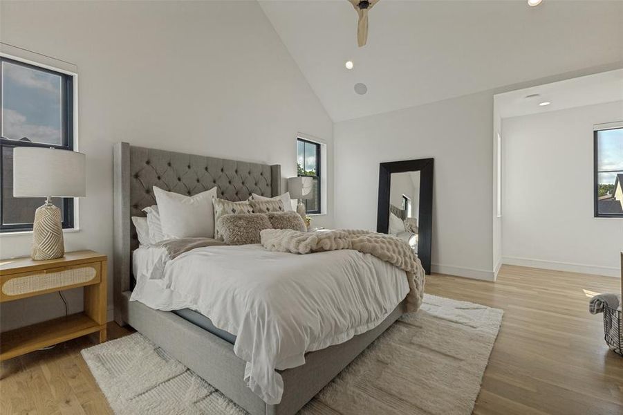 Spacious room featuring vaulted ceilings, light wood-finish flooring, recessed lighting, and multiple windows with dark frames Spacious room featuring vaulted ceilings, light wood-finish flooring, recessed lighting, and multiple windows with dark frames