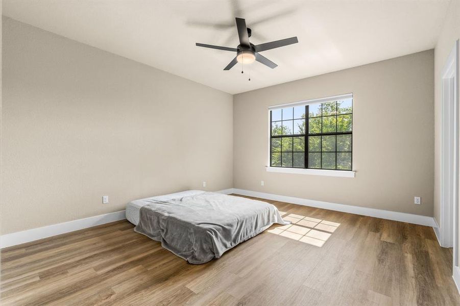 Spacious Secondary Primary Bedroom upstairs featuring wood-finish flooring, a large window with black grid panes, and a modern ceiling fan