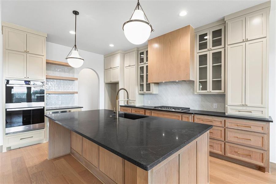 Kitchen featuring dark stone countertops, decorative backsplash, stainless steel appliances, a center island with sink, and light wood-style floors