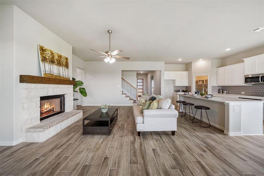 Living area featuring light wood-style flooring, ceiling fan, a stone fireplace, recessed lighting, and stairway Living area featuring light wood-style flooring, ceiling fan, a stone fireplace, recessed lighting, and stairway