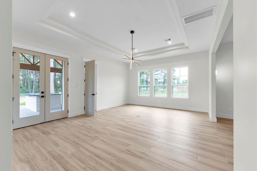 Bright and spacious room with light wood flooring, large windows, and French doors opening to the outdoors. Ideal for a living area with plenty of natural light and views of greenery.