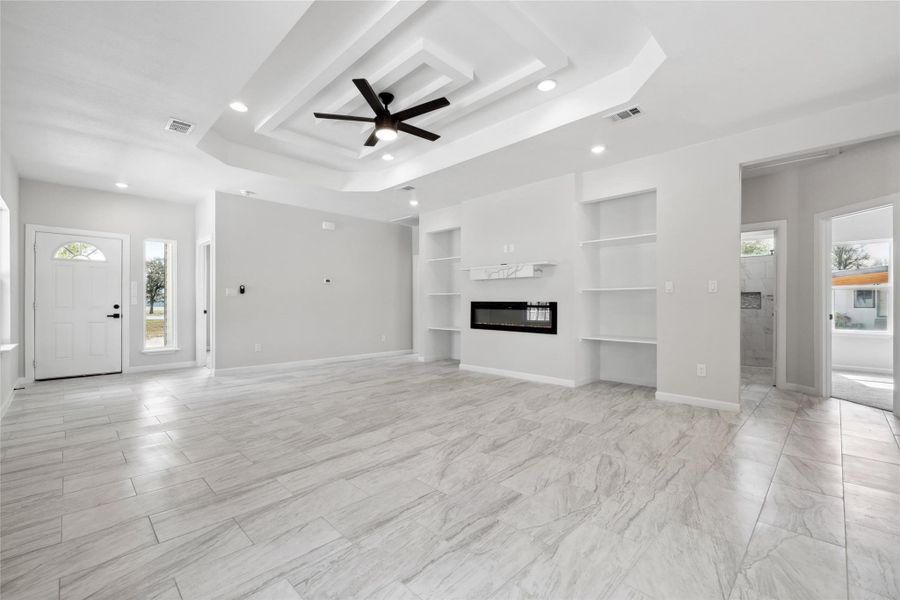 Unfurnished living room featuring healthy amount of natural light, a raised ceiling, built in features, recessed lighting, and ceiling fan Unfurnished living room featuring healthy amount of natural light, a raised ceiling, built in features, recessed lighting, and ceiling fan