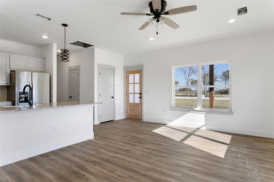 Kitchen with dark hardwood / wood-style floors, stainless steel fridge, ceiling fan, light stone counters, and white cabinetry