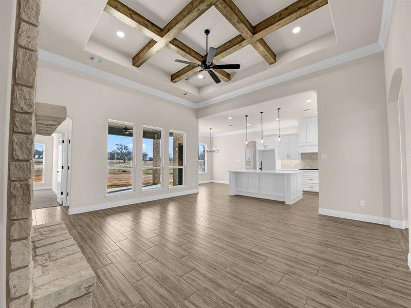 Unfurnished living room with beamed ceiling, ceiling fan with notable chandelier, coffered ceiling, a high ceiling, and crown molding