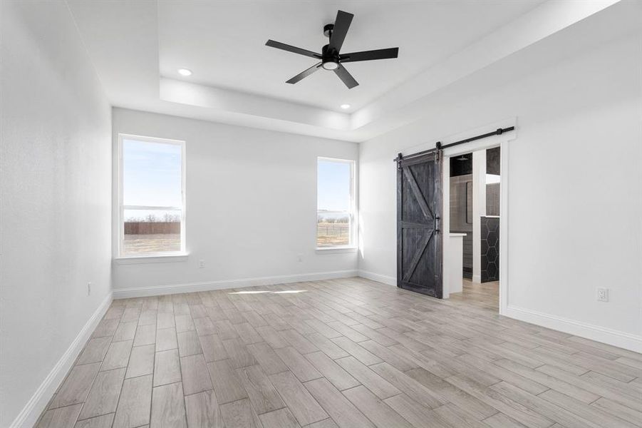 Unfurnished bedroom featuring multiple windows, a barn door, a raised ceiling, and light wood-type flooring