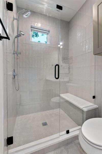 Primary bathroom featuring a walk-in shower featuring a frameless glass enclosure, white rectangular subway tile, a built-in shower bench, a rain shower head, and an additional handheld shower fixture Primary bathroom featuring a walk-in shower featuring a frameless glass enclosure, white rectangular subway tile, a built-in shower bench, a rain shower head, and an additional handheld shower fixture