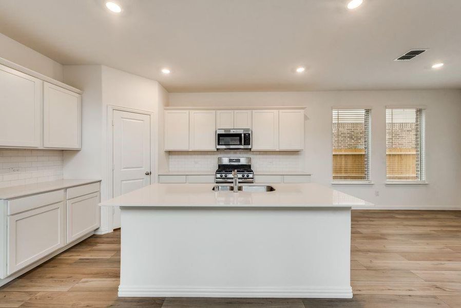 Kitchen featuring a center island with sink, decorative backsplash, white cabinets, and stainless steel appliances