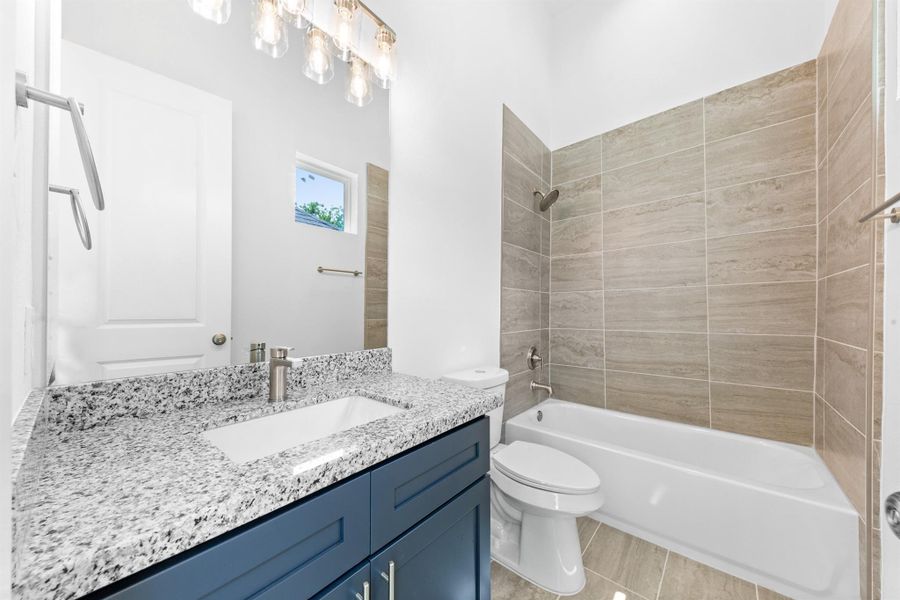 Bathroom features a tub/shower combo with sleek tile surround and modern fixtures, offering practical functionality and clean lines.