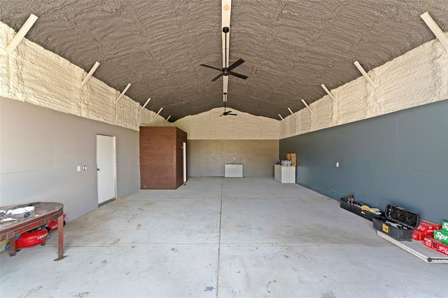 Misc room with unfinished concrete flooring, a ceiling fan, lofted ceiling, and a garage Misc room with unfinished concrete flooring, a ceiling fan, lofted ceiling, and a garage