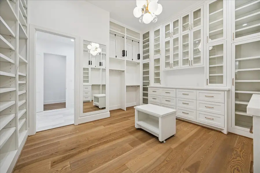 Custom cabinetry, abundant shelving, and seasonal rods create a boutique-style dressing space. A Visual Comfort chandelier and white oak details elevate the experience.
