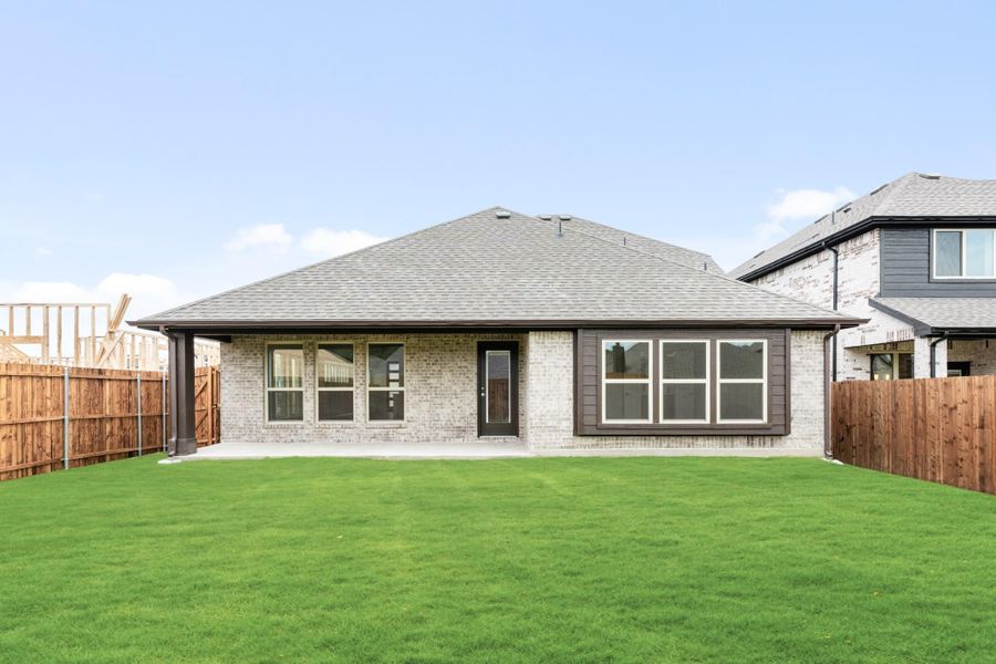 Rear exterior of single-story brick home with gray roof, patio, and fenced green backyard
