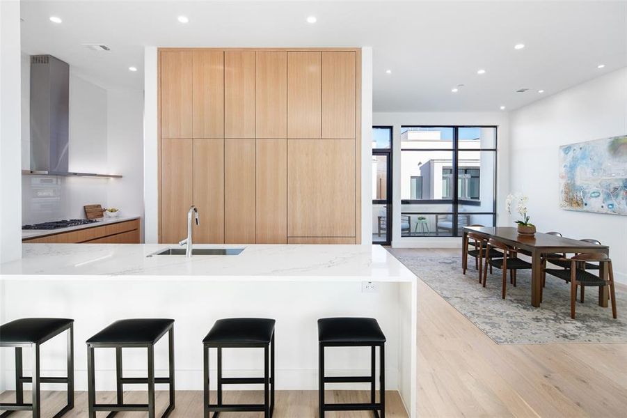 Kitchen featuring a kitchen breakfast bar, light stone countertops, wall chimney range hood, and light wood-type flooring