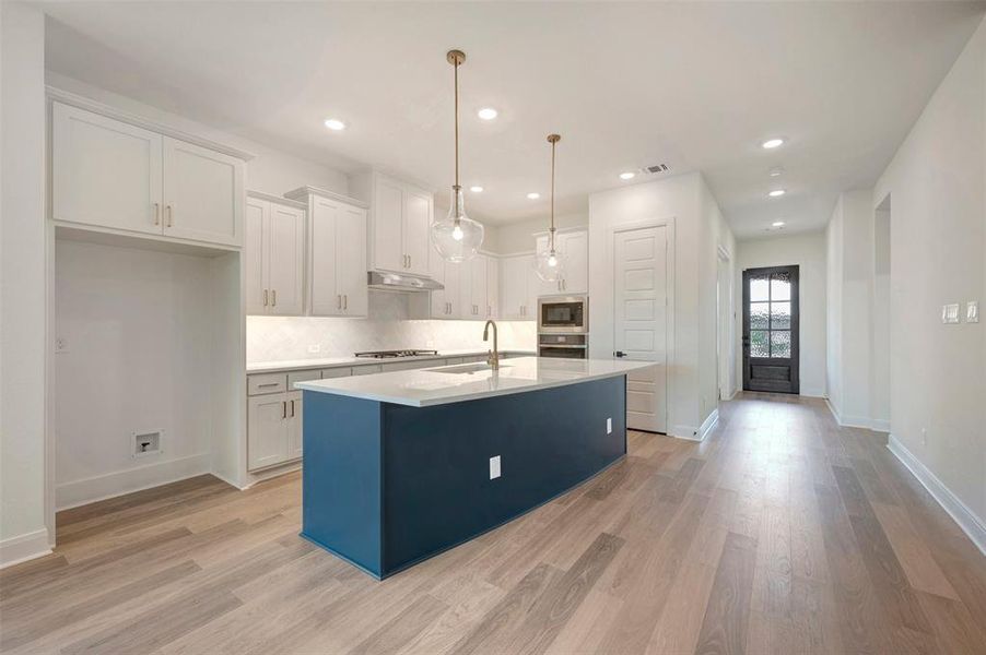 Modern kitchen featuring light wood flooring, white cabinetry, and a contrasting blue kitchen island with a white countertop