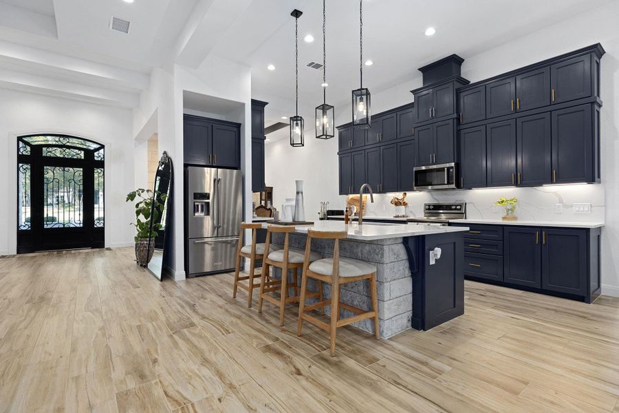 Kitchen with pendant lighting, stainless steel appliances, a kitchen island with sink, a kitchen breakfast bar, and light wood-style floors Kitchen with pendant lighting, stainless steel appliances, a kitchen island with sink, a kitchen breakfast bar, and light wood-style floors
