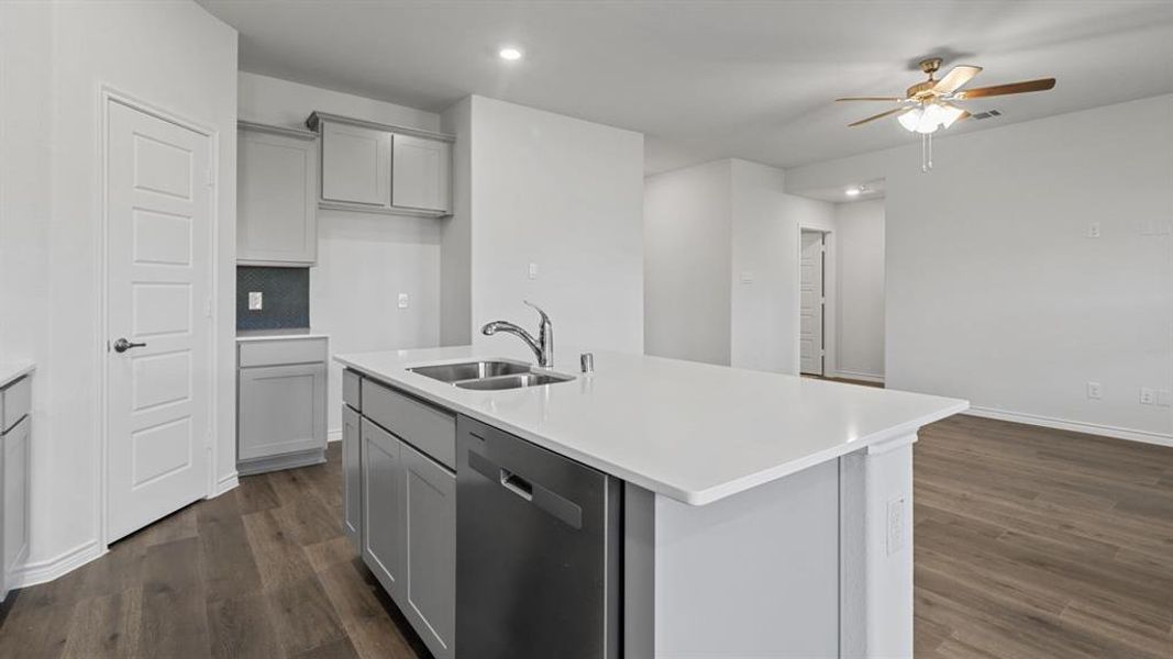 Kitchen featuring gray cabinetry, stainless steel dishwasher, an island with sink, dark wood-style flooring, and a ceiling fan