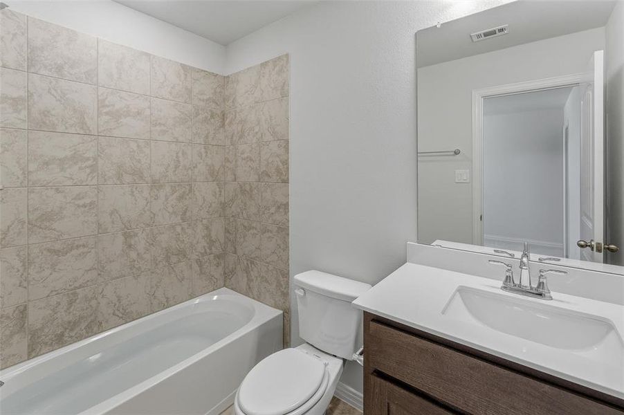 Full bathroom featuring a white tub, light-toned tiled bath surround, a vanity with a dark wood-finish cabinet, a white countertop, and an integrated sink with a chrome faucet