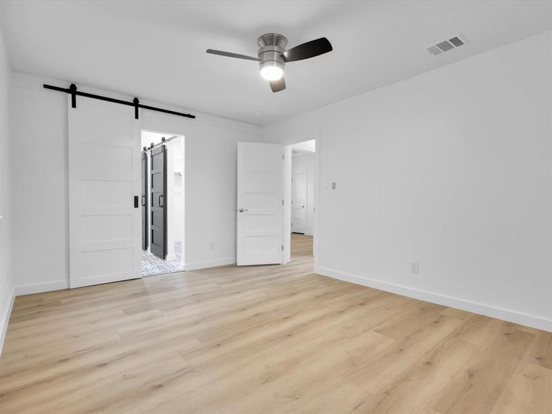 Spare room with light wood-type flooring, a barn door, and ceiling fan