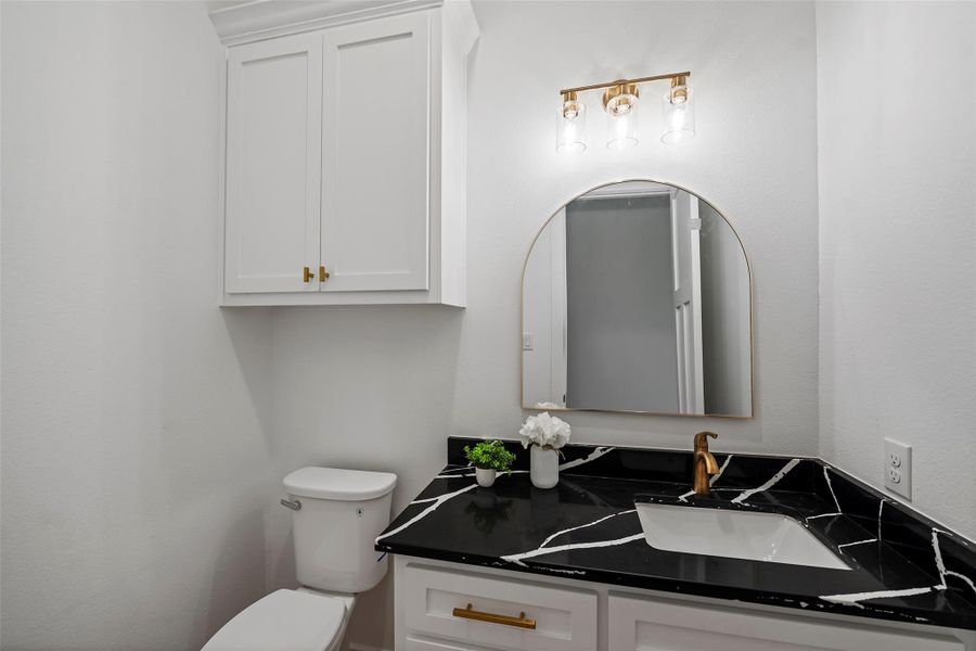 Stylish half bath featuring elegant black countertops, modern fixtures, and ample storage.