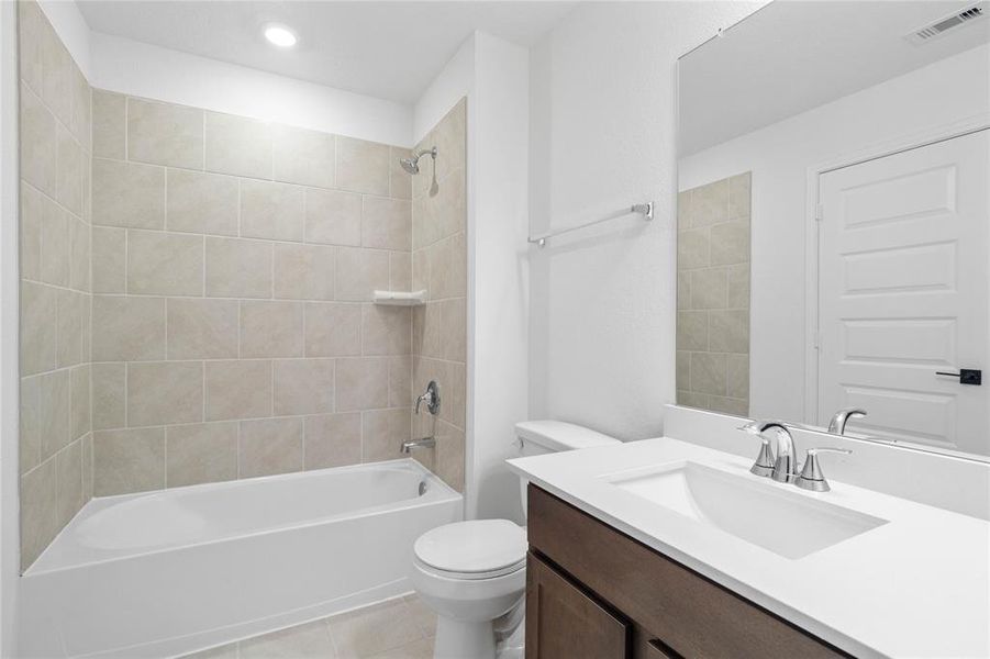 Secondary bath features tile flooring, tub/shower combo with tile surround, stained wood cabinets, beautiful light countertops, mirror, sleek fixtures and modern finishes.