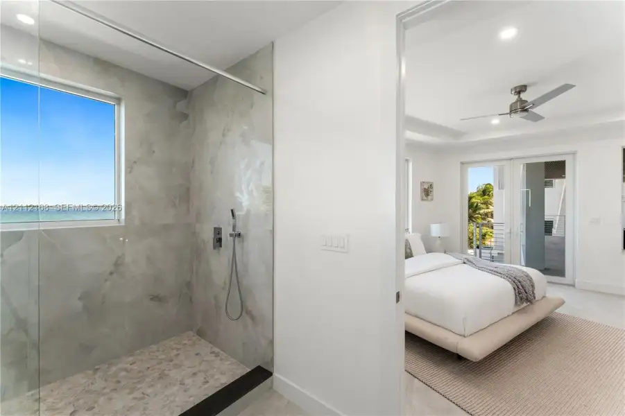 Walk-in shower featuring large-format tile surround, integrated window, handheld showerhead, pebble-finish flooring, and a frameless glass partition Walk-in shower featuring large-format tile surround, integrated window, handheld showerhead, pebble-finish flooring, and a frameless glass partition