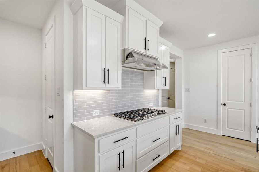 Kitchen with white cabinets, light stone countertops, light wood-type flooring, recessed lighting, and stainless steel gas stovetop