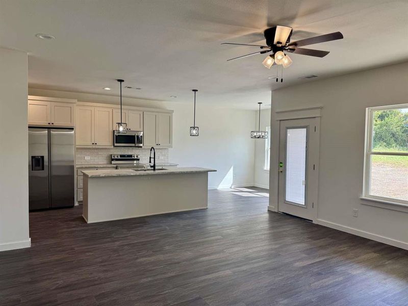 Kitchen with appliances with stainless steel finishes, a kitchen island with sink, backsplash, open floor plan, and dark wood-style floors Kitchen with appliances with stainless steel finishes, a kitchen island with sink, backsplash, open floor plan, and dark wood-style floors