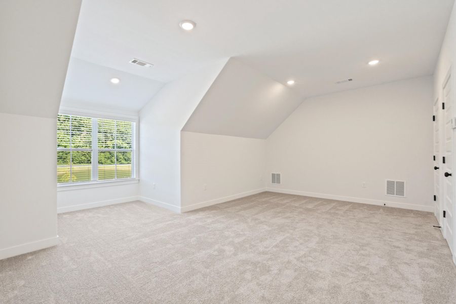 Recessed ceiling lighting, vaulted ceiling, neutral tone carpeting, double windows with blinds, and white paneled doors with black hardware Recessed ceiling lighting, vaulted ceiling, neutral tone carpeting, double windows with blinds, and white paneled doors with black hardware