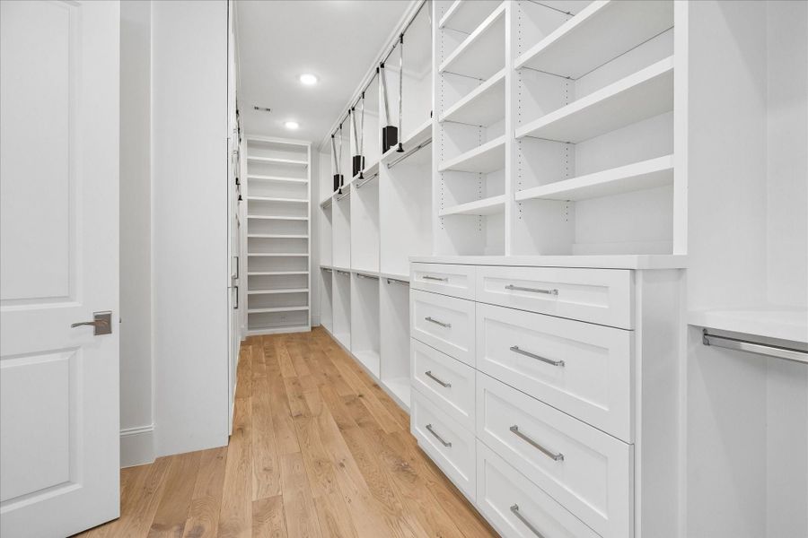 Spacious primary closet features built-in storage and ample room for hanging clothes with pull-down bars for accessing all custom storage solutions.