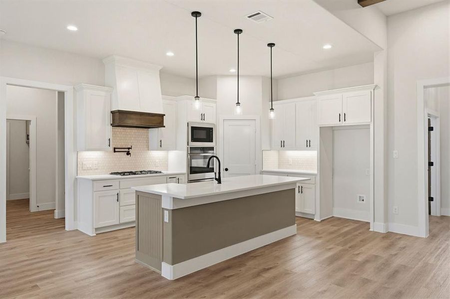 Spacious kitchen featuring an island with pendant lighting, white shaker cabinetry, stainless steel appliances, and wood-finish flooring