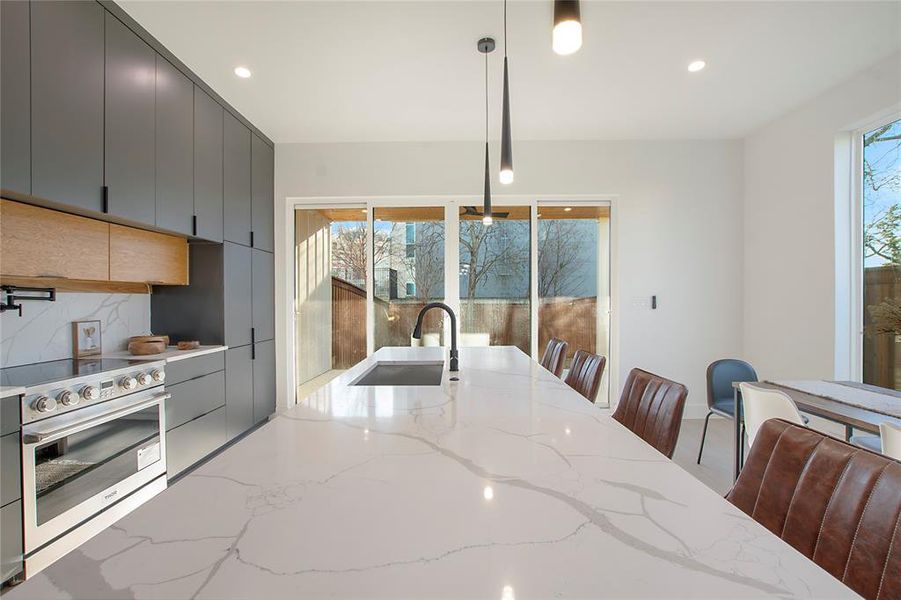 Kitchen with gray cabinetry, sink, hanging light fixtures, decorative backsplash, and high end stove