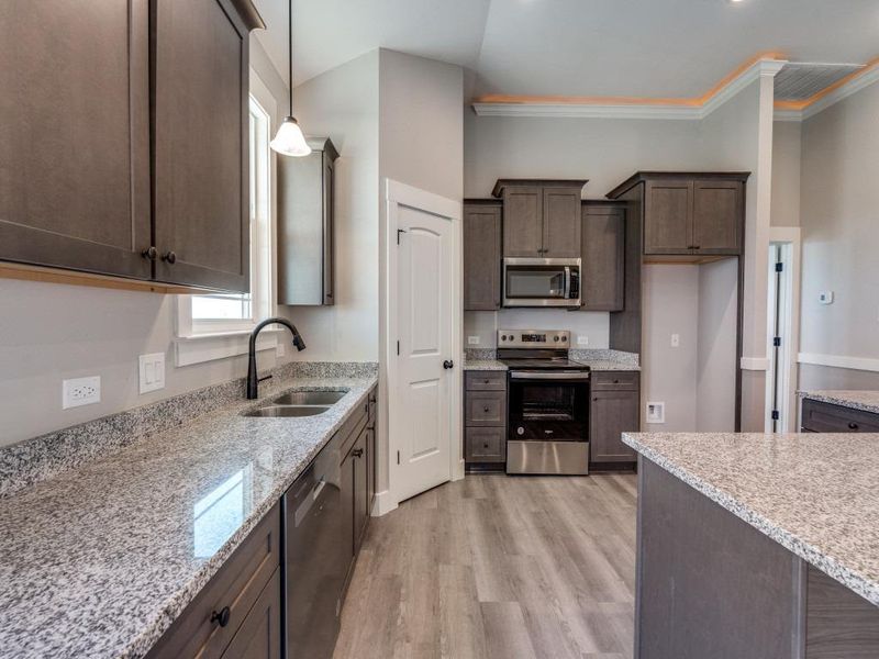 Kitchen featuring crown molding, a sink, light wood-style floors, dark brown cabinetry, and appliances with stainless steel finishes