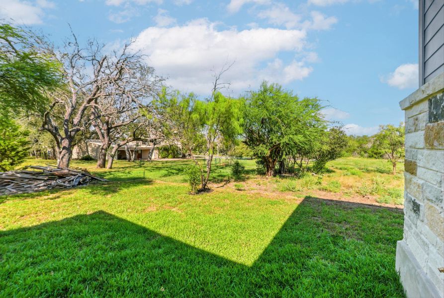 A spacious backyard featuring  a lush green lawn, surrounded by mature trees and natural landscaping
