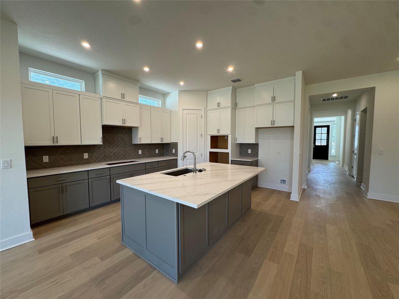 Two tone kitchen featuring two tone color scheme, light stone countertops, light wood-type flooring, an island with sink, and backsplash