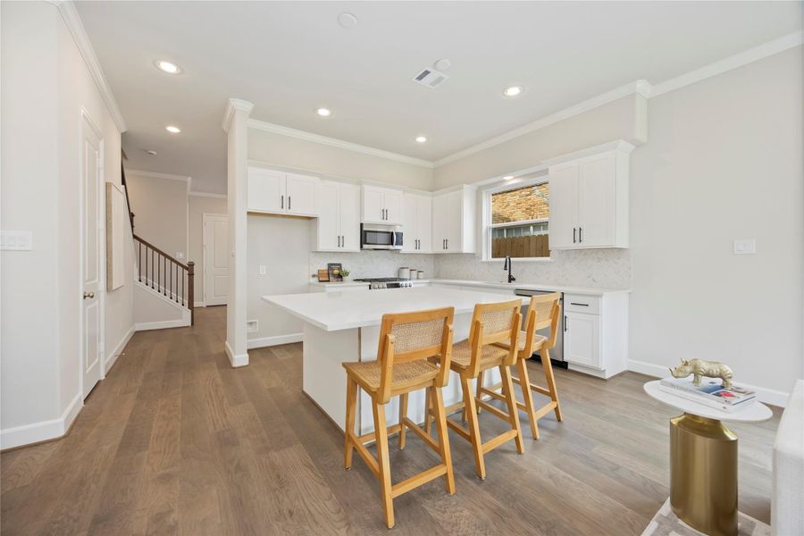An alternate view unveils the kitchen’s grand island, serving as the heart of the home, with an inviting passage to the adjacent dining room, where memories await to be made.