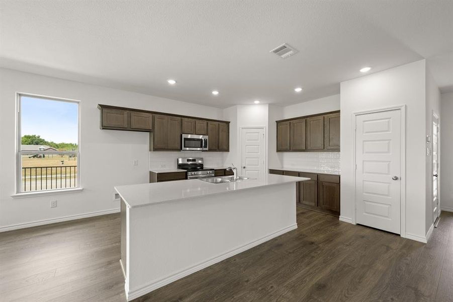 Kitchen featuring dark wood-type flooring, tasteful backsplash, appliances with stainless steel finishes, and a kitchen island with sink