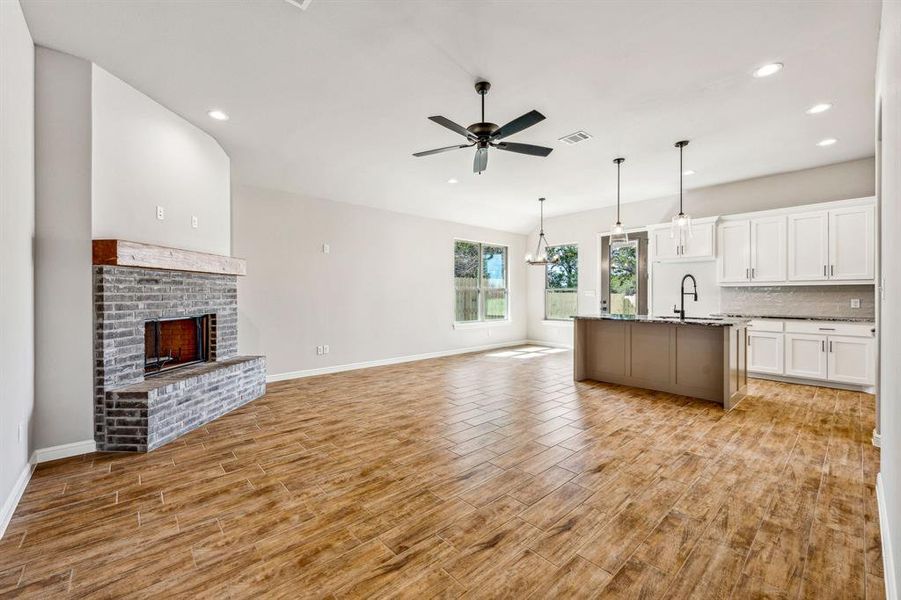 Kitchen with a fireplace, ceiling fan with notable chandelier, light hardwood / wood-style floors, white cabinetry, and a center island with sink