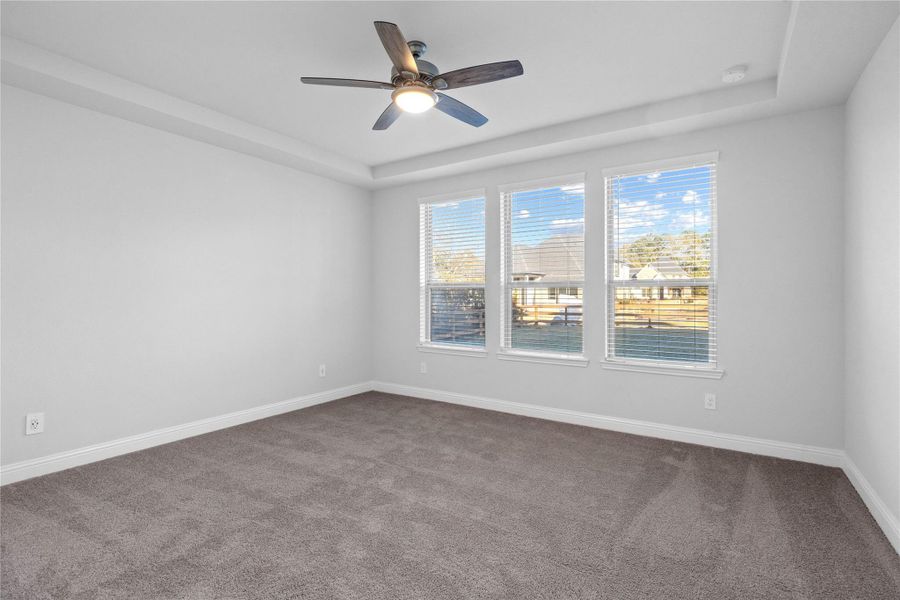 This spacious primary bedroom is an ideal private retreat, offering abundant natural light through multiple large windows and year-round comfort with a modern ceiling fan. The neutral color palette, including soft gray carpeting, creates a calm and inviting atmosphere that provides a perfect blank canvas for new owners to personalize. This spacious primary bedroom is an ideal private retreat, offering abundant natural light through multiple large windows and year-round comfort with a modern ceiling fan. The neutral color palette, including soft gray carpeting, creates a calm and inviting atmosphere that provides a perfect blank canvas for new owners to personalize.