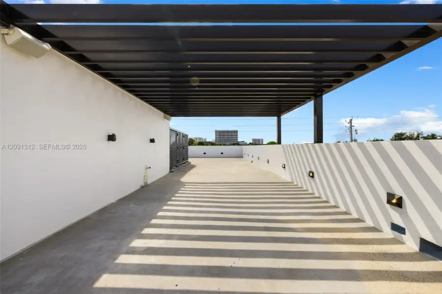 Rooftop terrace featuring a black metal pergola, concrete flooring, exterior wall-mounted lighting, and solid perimeter walls Rooftop terrace featuring a black metal pergola, concrete flooring, exterior wall-mounted lighting, and solid perimeter walls