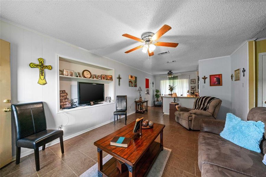 Living room with ceiling fan, ornamental molding, a textured ceiling, and tile patterned flooring
