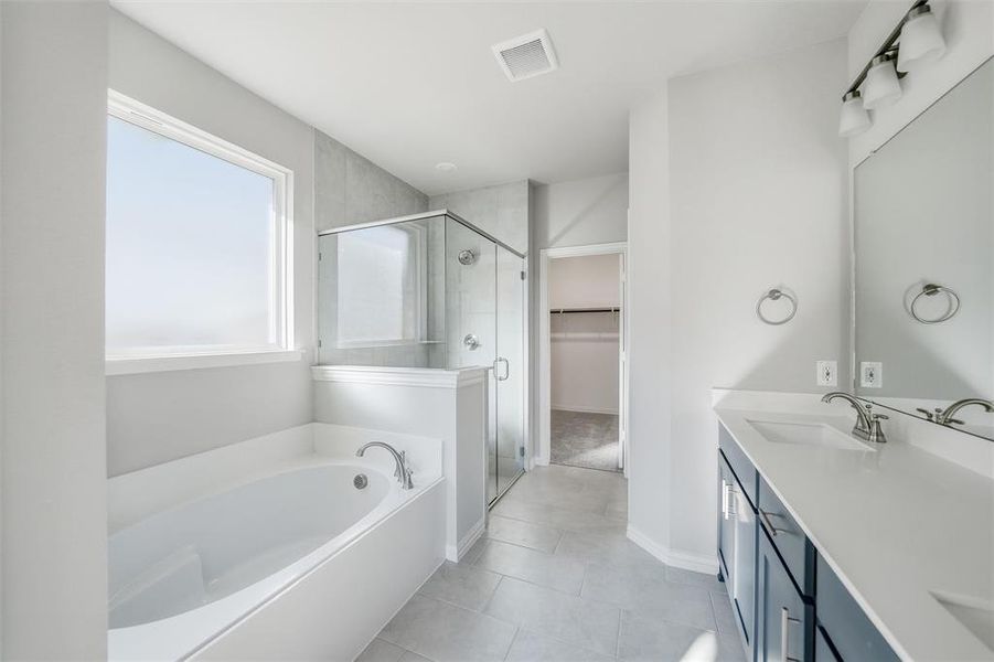 Full bathroom featuring double vanity, a garden tub, a spacious closet, a shower stall, and light tile patterned flooring Full bathroom featuring double vanity, a garden tub, a spacious closet, a shower stall, and light tile patterned flooring