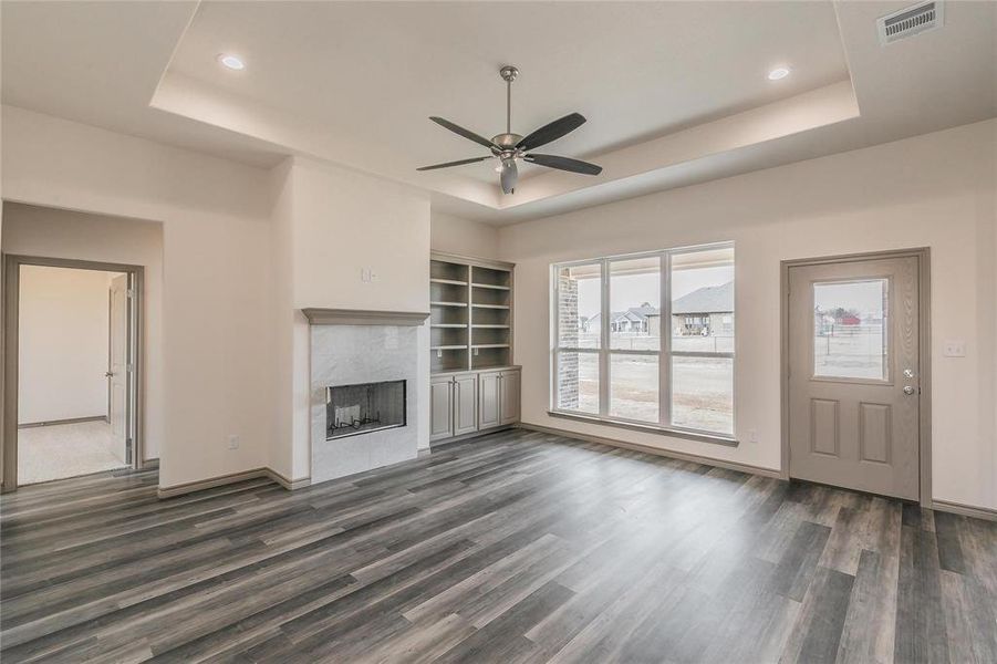 Unfurnished living room with a raised ceiling, dark wood-style floors, a fireplace, and ceiling fan