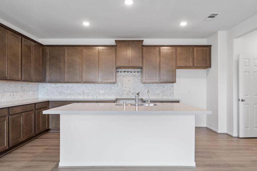 This light and bright kitchen features a large quartz island, white cabinets, a large sink overlooking your family room, recessed lighting, and beautiful backsplash.
